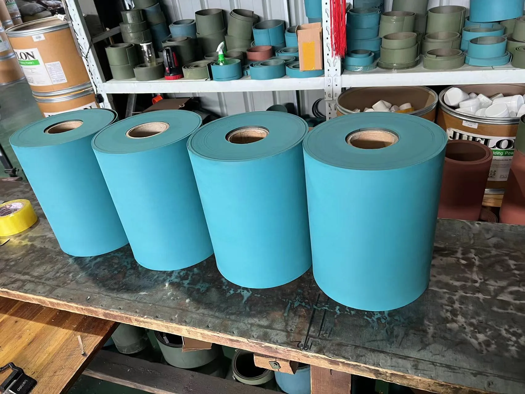 Four large rolls of blue Turcite B sheet on a bench, with further rolls shelved behind.