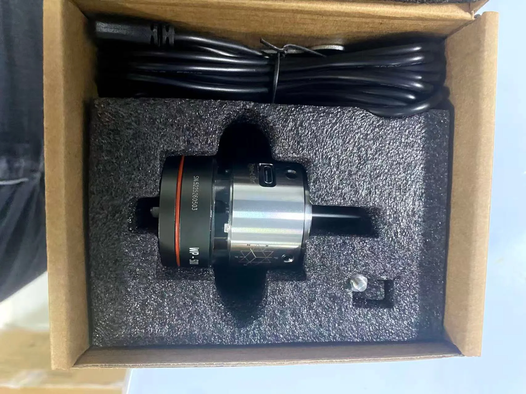 A machining-centre touch probe resting in its foam packing with its connecting cable coiled above it.