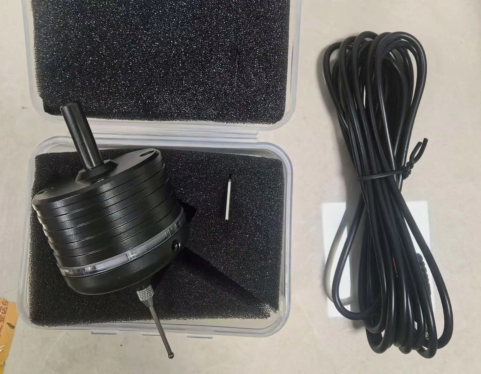 A black 3D touch probe next to a clear case holding its stylus, with a coiled connecting cable.